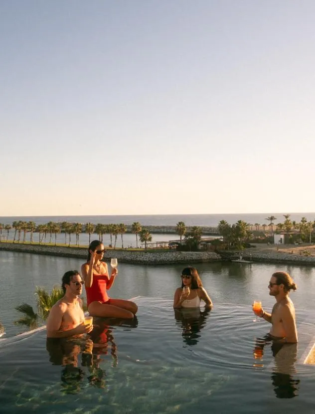Des personnes se détendent dans une piscine avec vue sur la mer et la végétation.