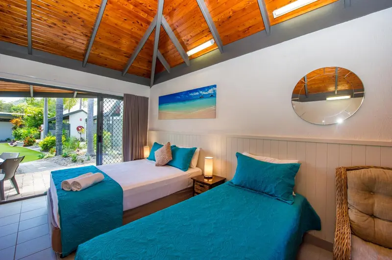 Chambre lumineuse avec deux lits simples et vue sur un jardin tropical.