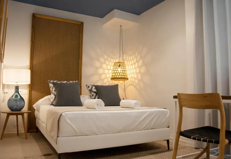 Une chambre lumineuse avec un lit blanc et des coussins gris.