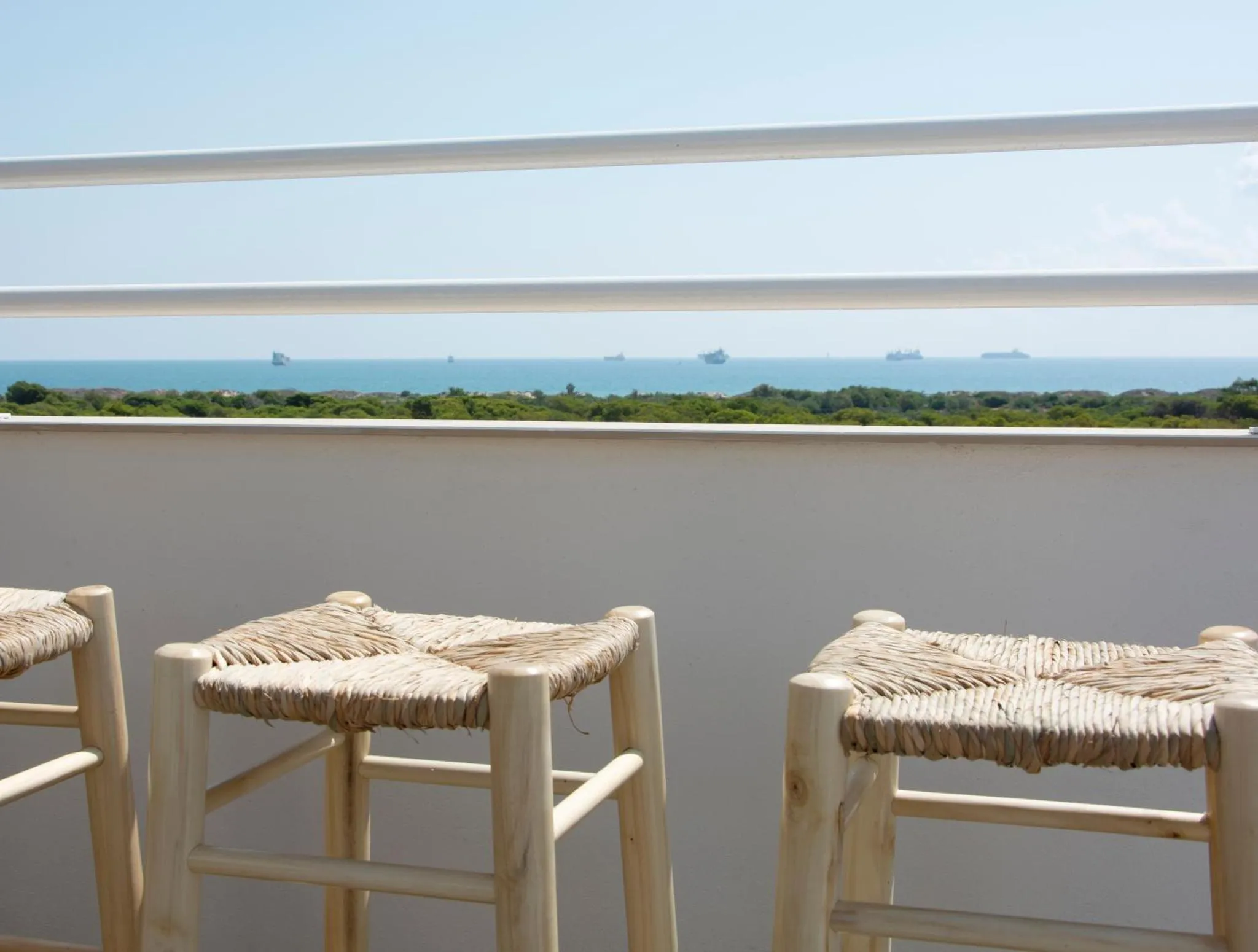 Tabourets en osier sur une terrasse avec vue sur la mer et la côte.