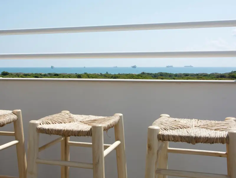 Tabourets en osier sur une terrasse avec vue sur la mer et la côte.