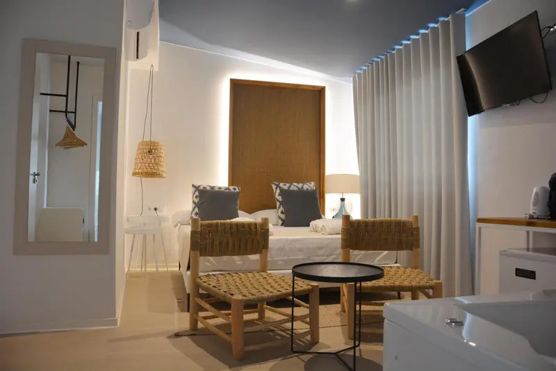Chambre lumineuse avec un lit et des fauteuils en rotin.