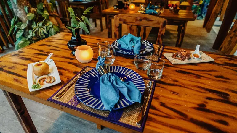 Une table en bois est dressée pour un repas avec des assiettes décorées et des couverts.