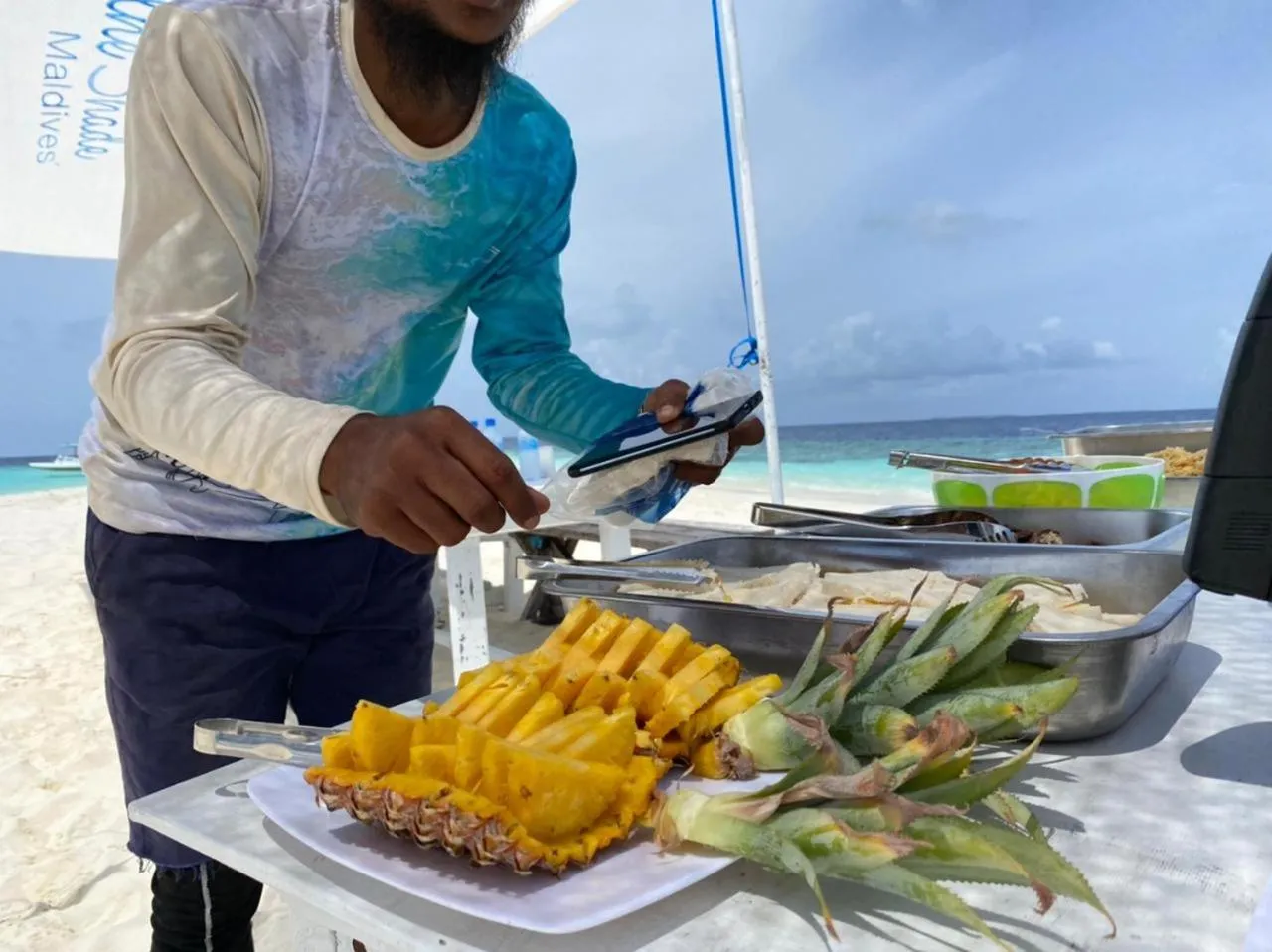 Un homme prépare des fruits frais sur une table en bord de mer.