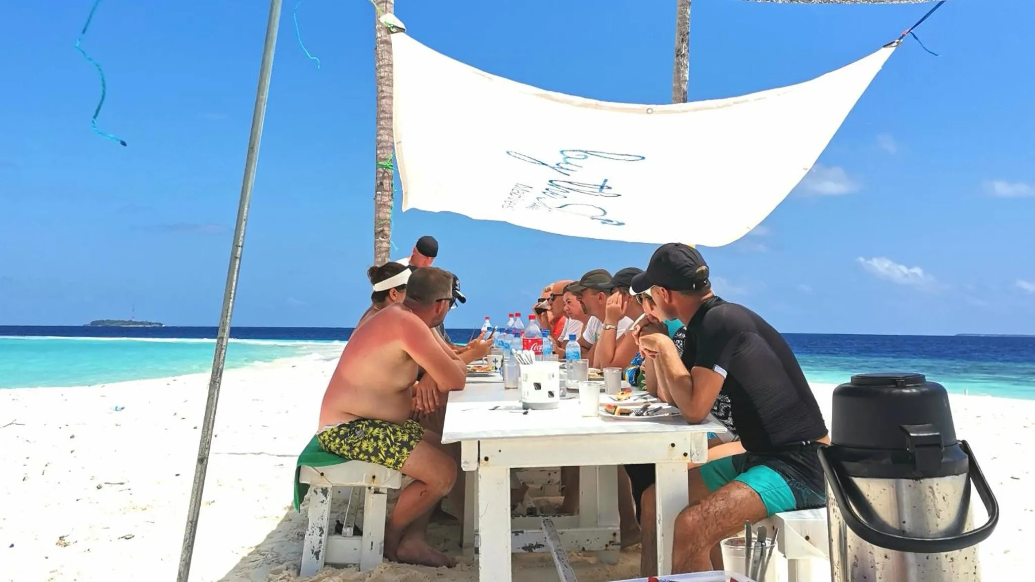 Des personnes sont assises à une table sur une plage de sable blanc face à la mer.