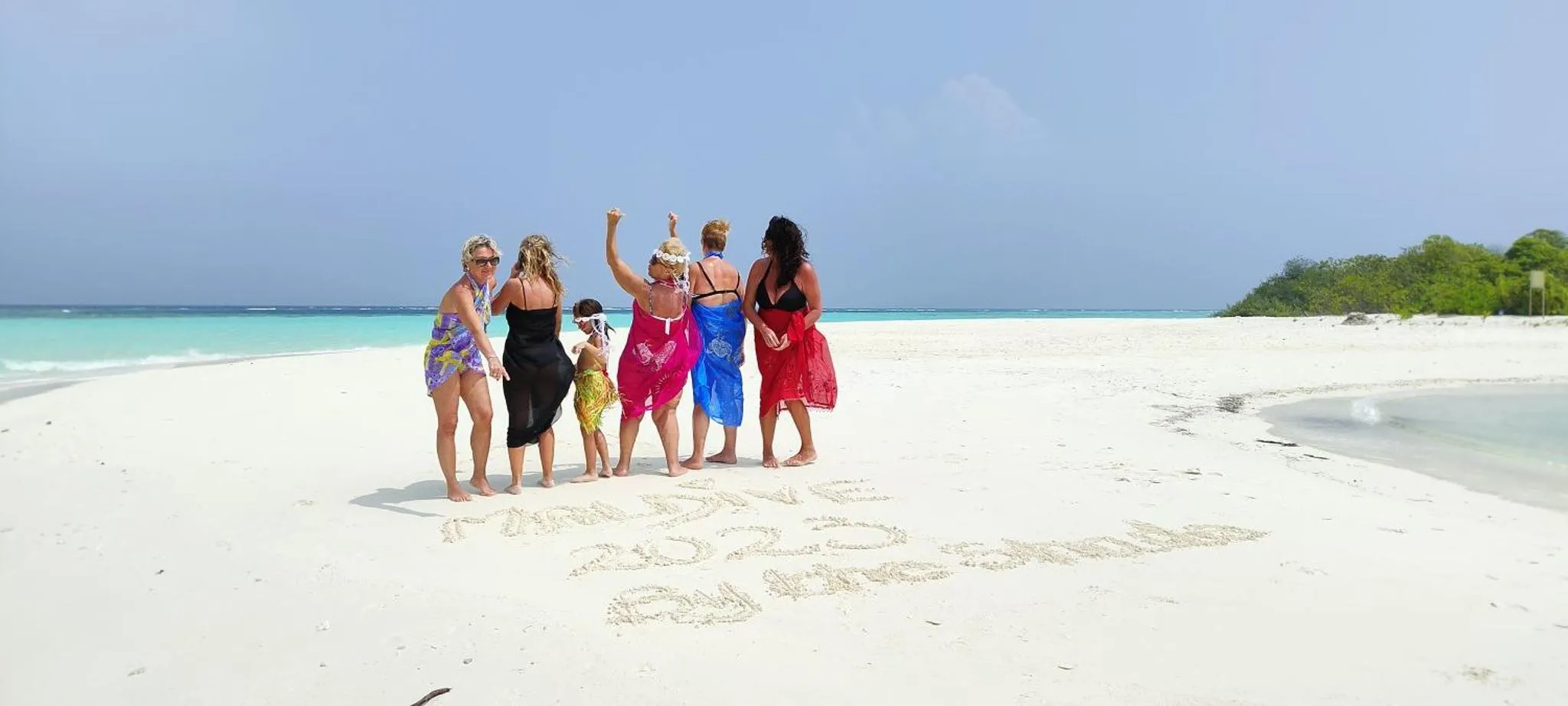 Groupe de personnes se tenant sur une plage de sable blanc face à la mer.
