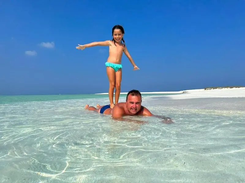 Un homme et une enfant s'amusent dans une eau turquoise peu profonde.