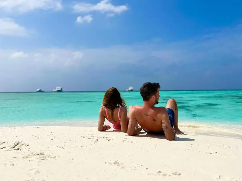 Deux personnes se relaxent sur une plage de sable blanc face à une mer turquoise.