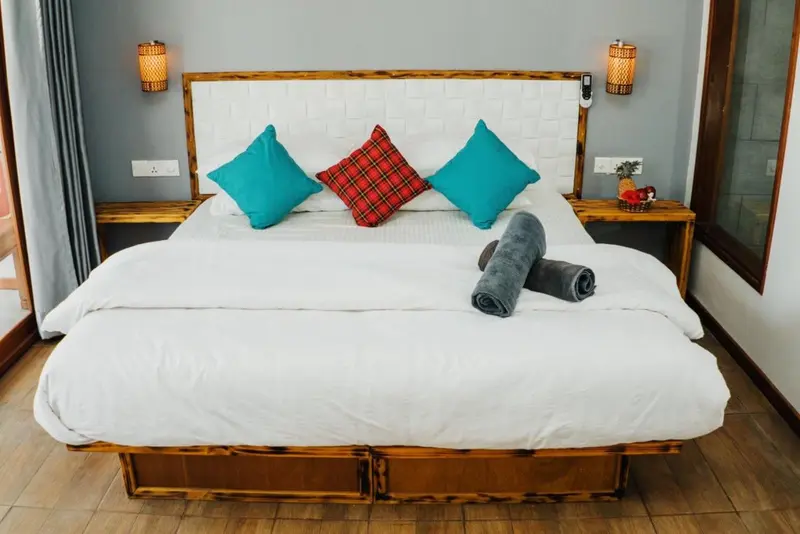 Un lit double est dispose dans une chambre lumineuse avec des oreillers turquoise et rouges.
