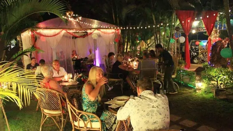 Une terrasse illuminée accueille des convives autour de tables décorées.