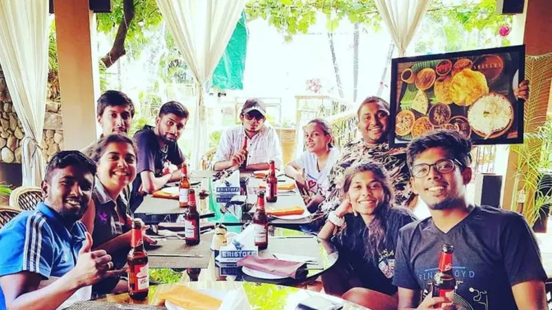 Un groupe de personnes souriantes est assis autour d'une table en extérieur avec des boissons et de la nourriture.