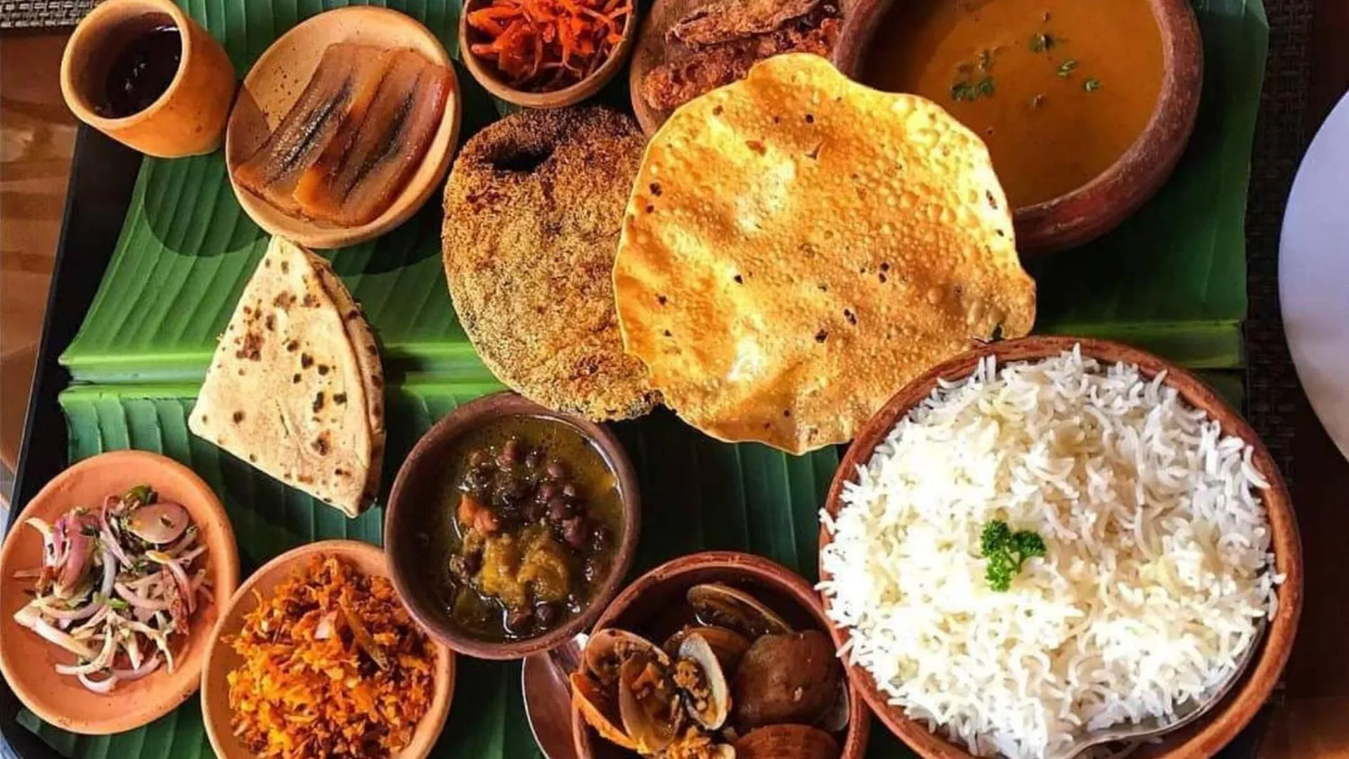 Assortiment de plats traditionnels servis dans des récipients en terre cuite sur un plateau en feuilles de bananier.