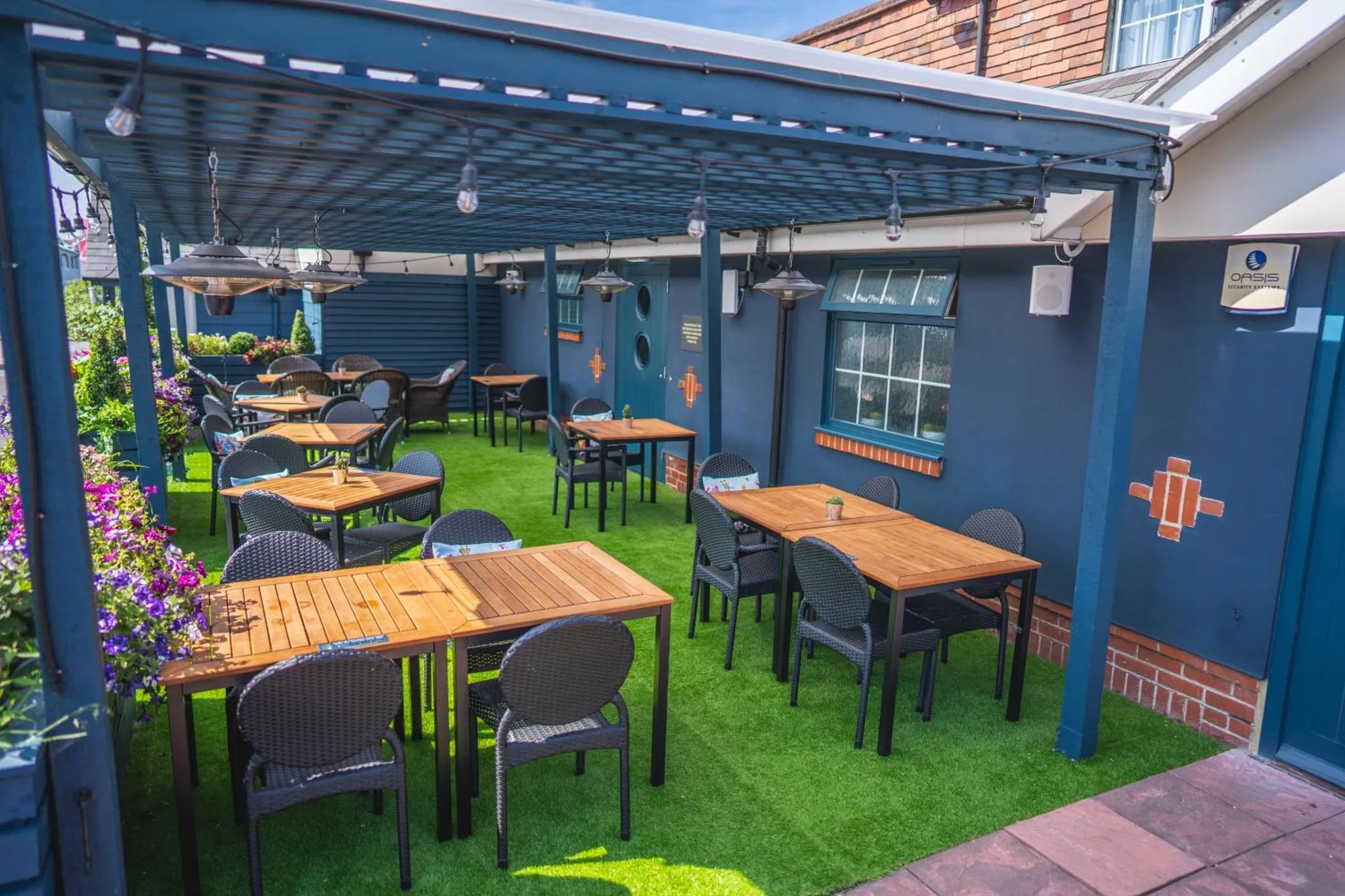 Terrasse ombragée avec tables et chaises en bois sur un sol vert.