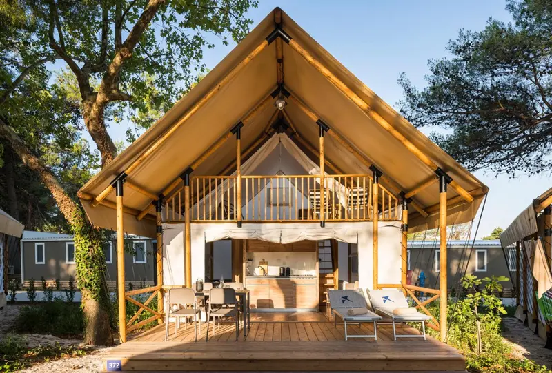 Tente lodge avec terrasse en bois et mobilier de jardin.