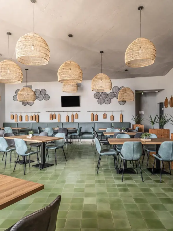 Une salle de restaurant lumineuse avec des tables en bois et des chaises vertes.
