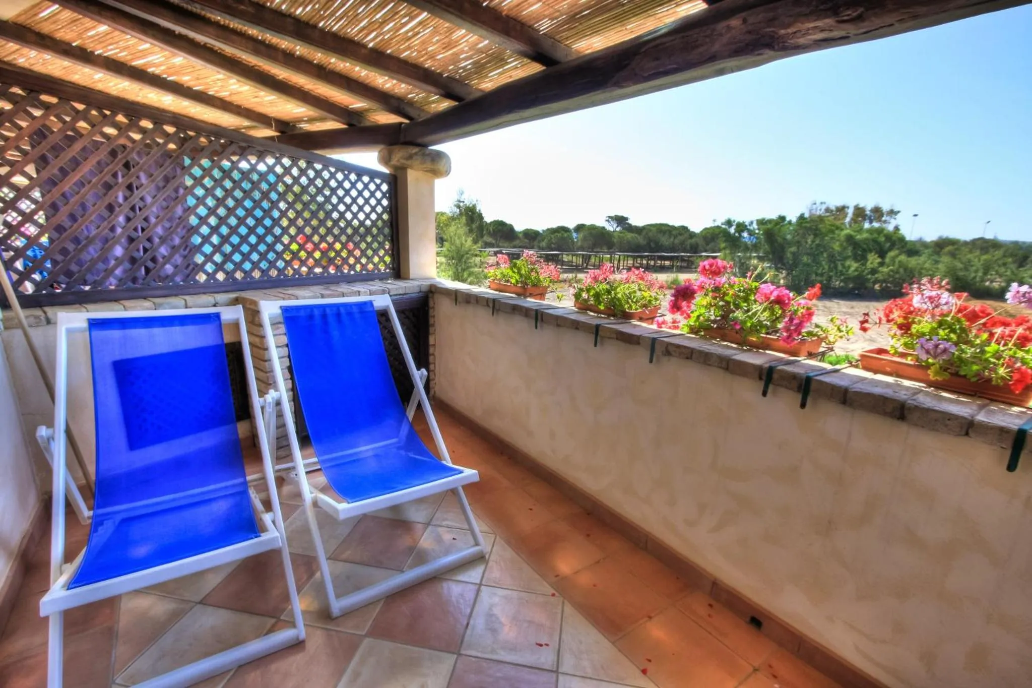 Deux transats bleus sur une terrasse carrelée fleurie avec vue sur la végétation.