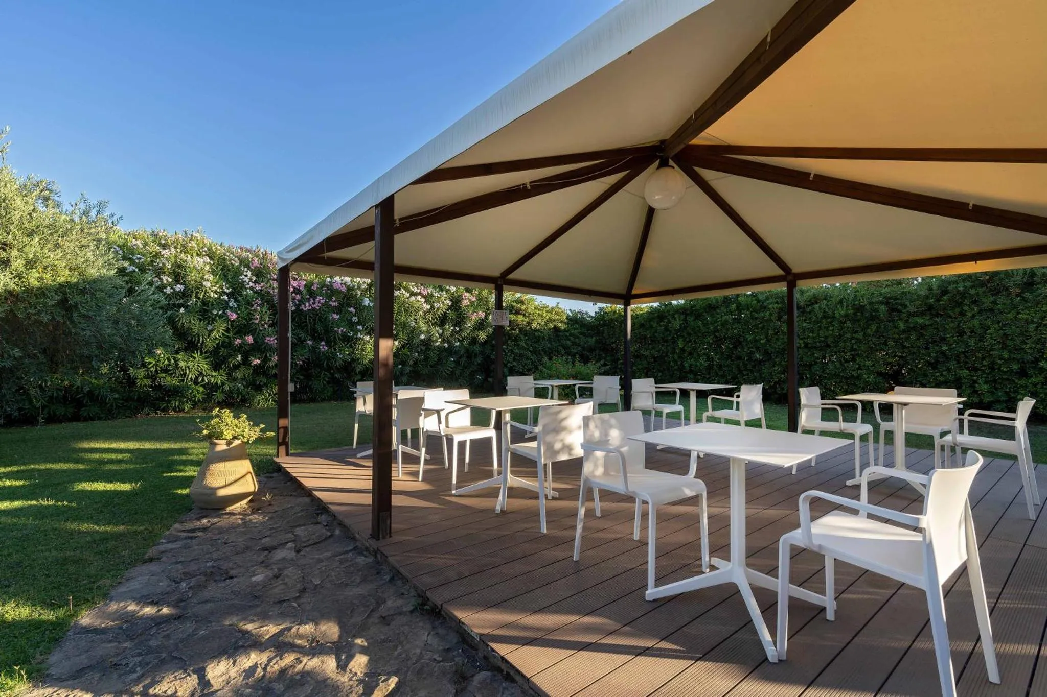 Terrasse ombragée avec tables et chaises blanches sur un sol en bois.
