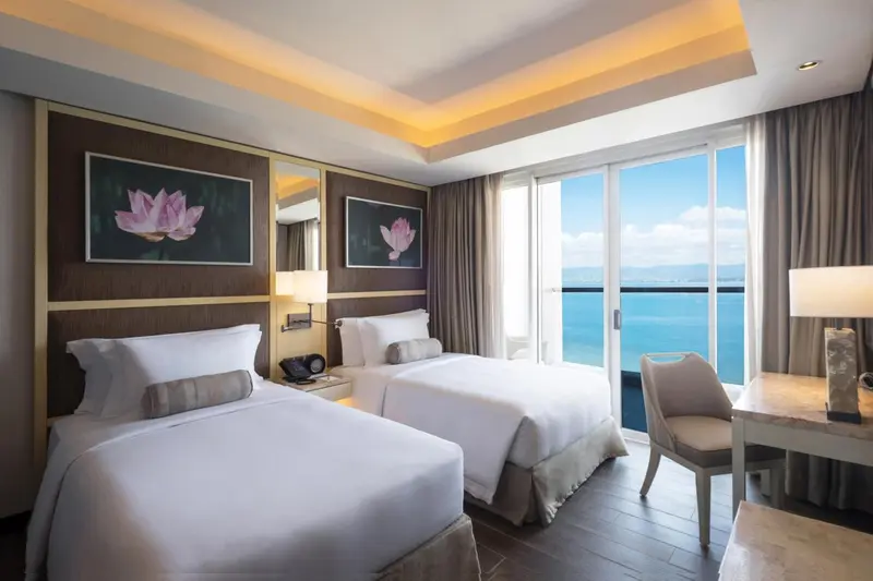 Chambre lumineuse avec deux lits simples et vue sur la mer.
