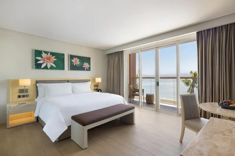 Une chambre lumineuse avec un grand lit et un accès à un balcon avec vue sur la mer.