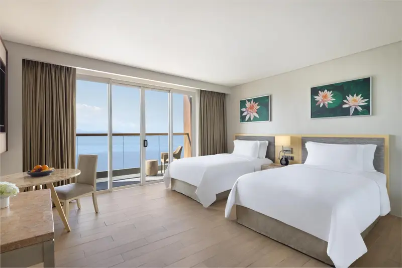 Chambre lumineuse avec deux lits simples et vue sur la mer.