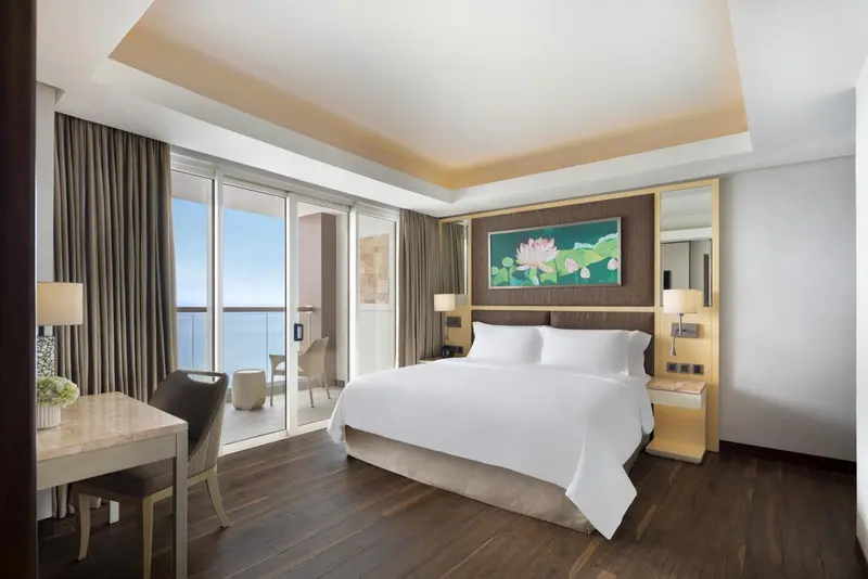 Chambre lumineuse avec un grand lit et un balcon donnant sur la mer.