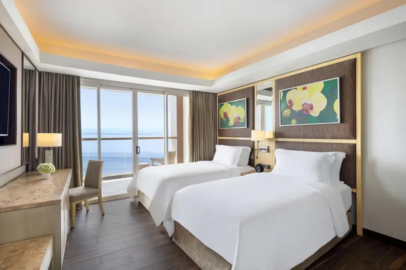Chambre lumineuse avec deux lits simples et vue sur la mer.