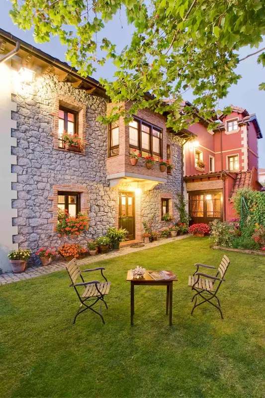 Façade en pierre avec balcon fleuri et mobilier de jardin sur pelouse.