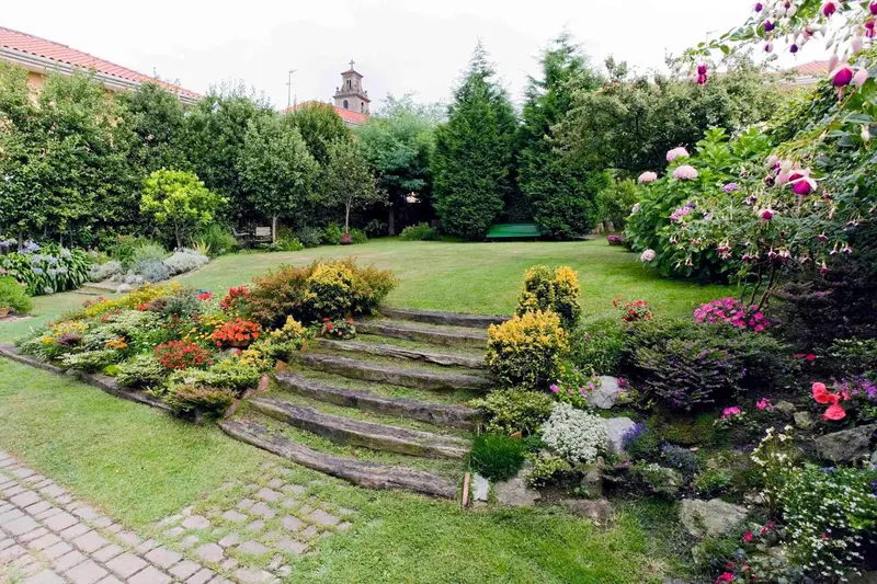 Un jardin verdoyant avec des parterres fleuris et des escaliers en pierre.