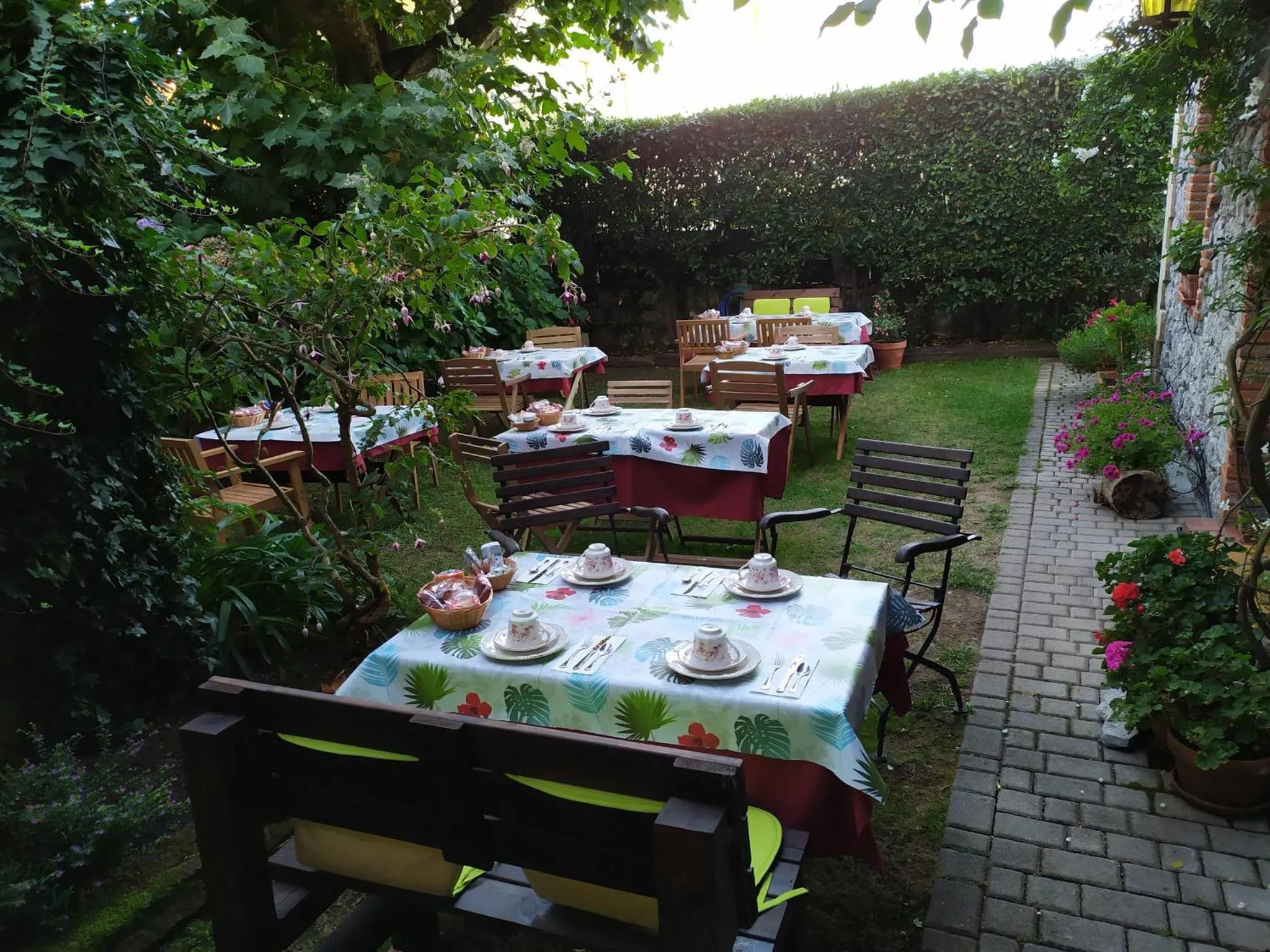 Tables dressées pour un repas en extérieur dans un jardin fleuri.