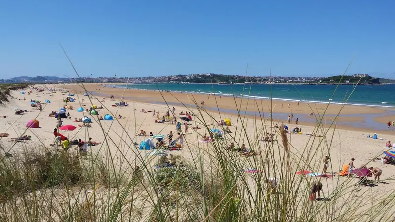 Une plage de sable fin avec des baigneurs et des parasols sous un ciel bleu.