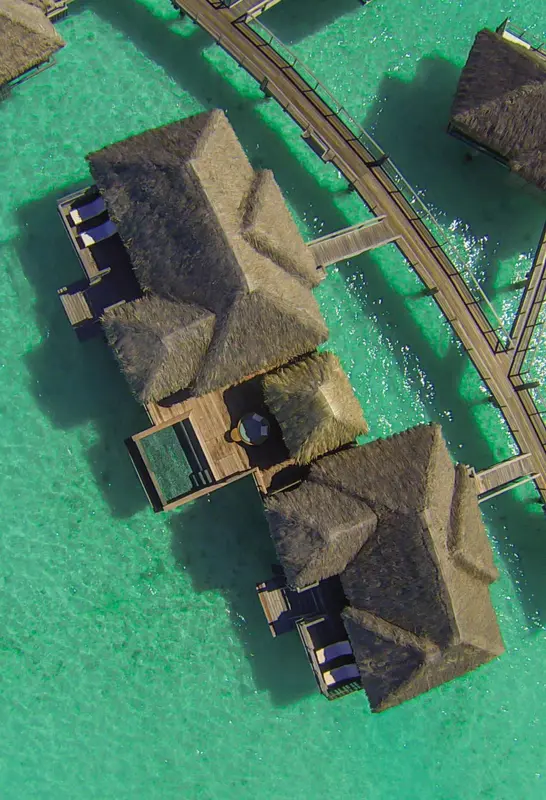 Vue aérienne de bungalows sur pilotis au-dessus d'une eau turquoise.