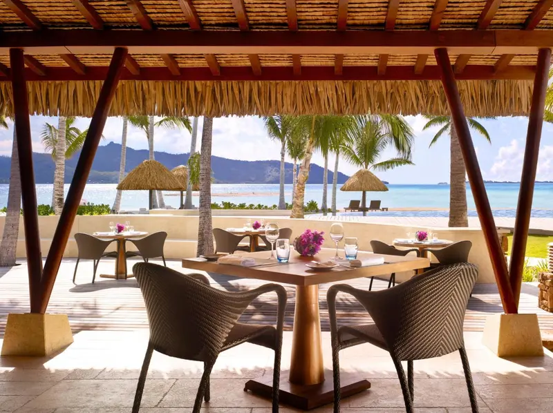 Tables dressées sur une terrasse ombragée face à la mer.