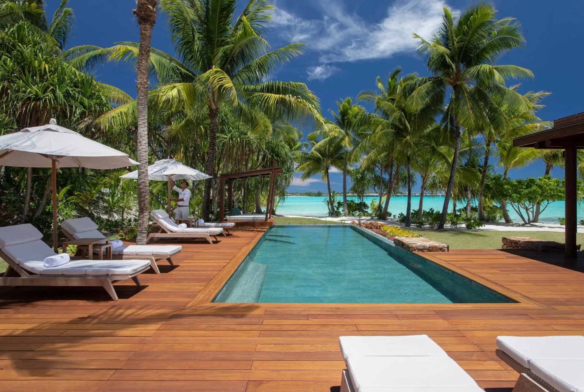 Transats blancs disposés autour d'une piscine rectangulaire turquoise, bordée d'une terrasse en bois.