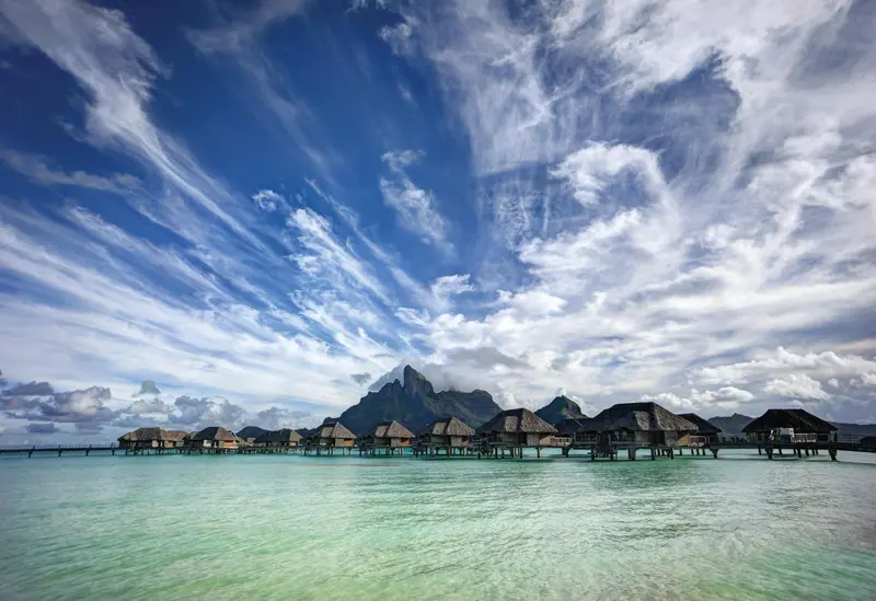 Cabanes sur pilotis au milieu d'une eau turquoise sous un ciel nuageux.