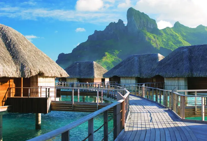 Des bungalows sur pilotis s'alignent sur une passerelle au-dessus d'une eau turquoise.