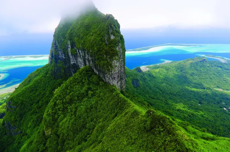 Vue aérienne d'une montagne verdoyante surplombant une lagune turquoise.