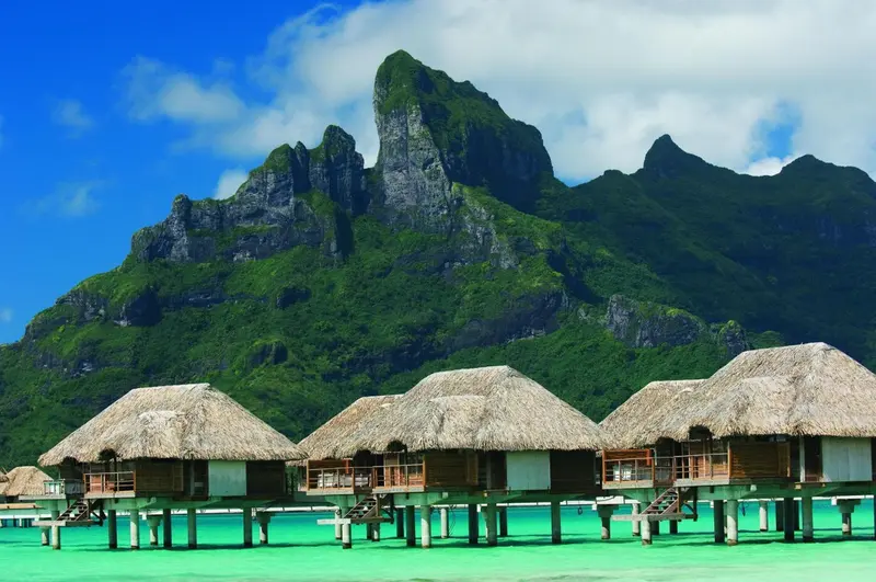 Des bungalows sur pilotis face à une montagne verdoyante.