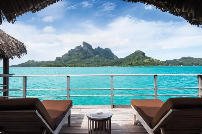 Terrasse en bois avec deux chaises longues donnant sur une mer turquoise et des montagnes verdoyantes.