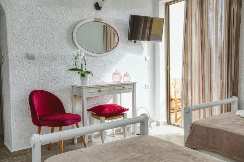 Une chambre lumineuse avec un lit, une coiffeuse et un fauteuil rouge.