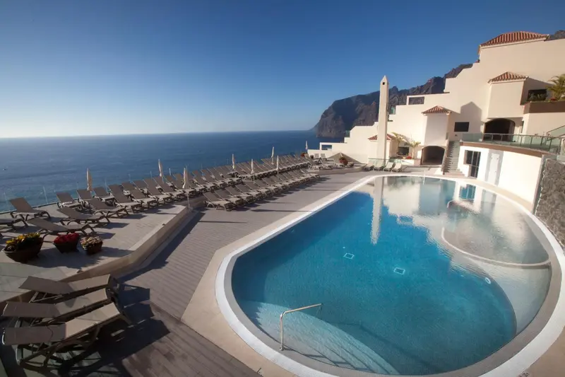 Une piscine avec des transats en bord de mer sous un ciel bleu.