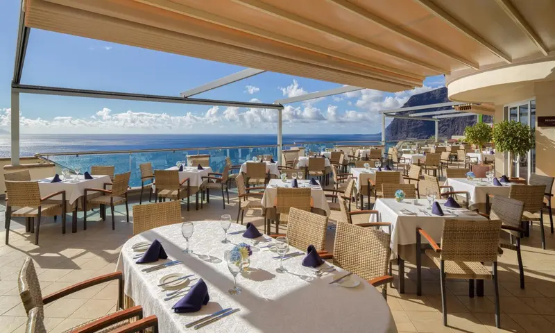 Terrasse ombragée avec tables dressées face à la mer.