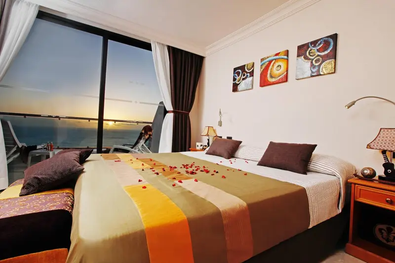 Une chambre avec un grand lit donnant sur une vue mer au coucher du soleil.