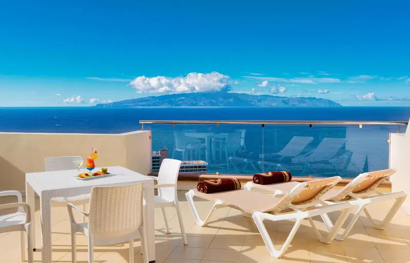 Terrasse avec table, chaises longues et vue sur la mer et une île.