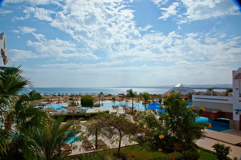 Vue aérienne sur un complexe hôtelier avec piscines et végétation luxuriante face à la mer.