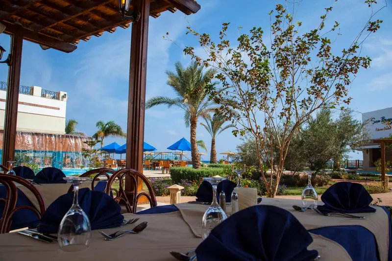 Une salle à manger extérieure avec des tables dressées et une vue sur une piscine et un jardin.