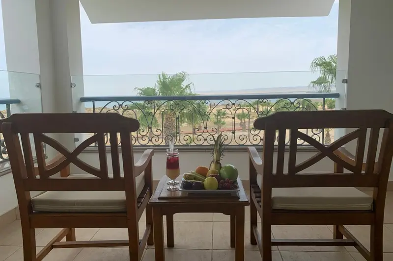Deux fauteuils en bois et une table basse avec des fruits frais sur une terrasse avec vue sur la mer.