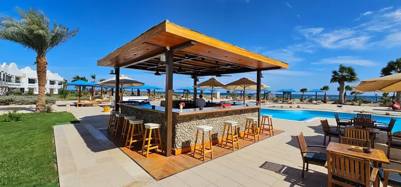 Un bar en plein air avec des tabourets et une piscine en arrière-plan.