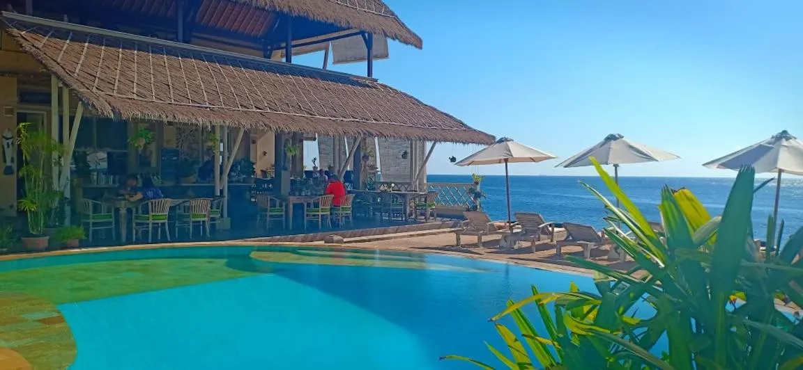 Terrasse avec piscine et vue sur la mer, ombragée par des parasols.