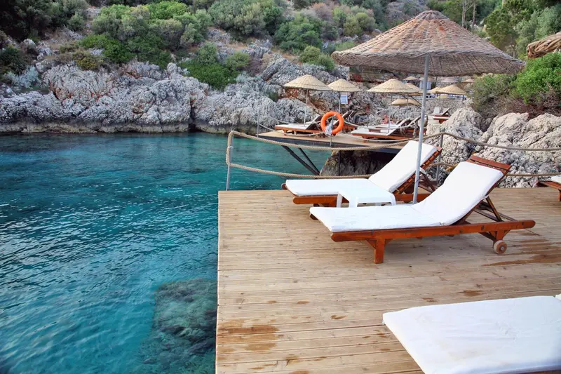 Transats blancs sur une terrasse en bois surplombant une eau turquoise.