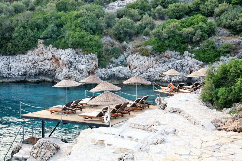 Transats et parasols sur une plateforme en bois au bord de l'eau turquoise.